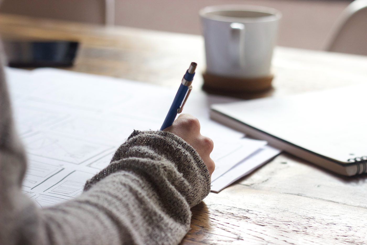 A person writing notes at a wooden desk beside a coffee cup