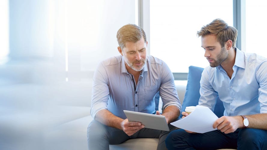 Two men reviewing investment documents on a couch in a bright office