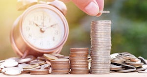 Stacked coins beside a clock representing savings over time