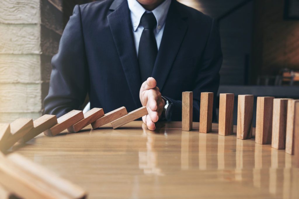 Businessman stopping falling wooden dominoes