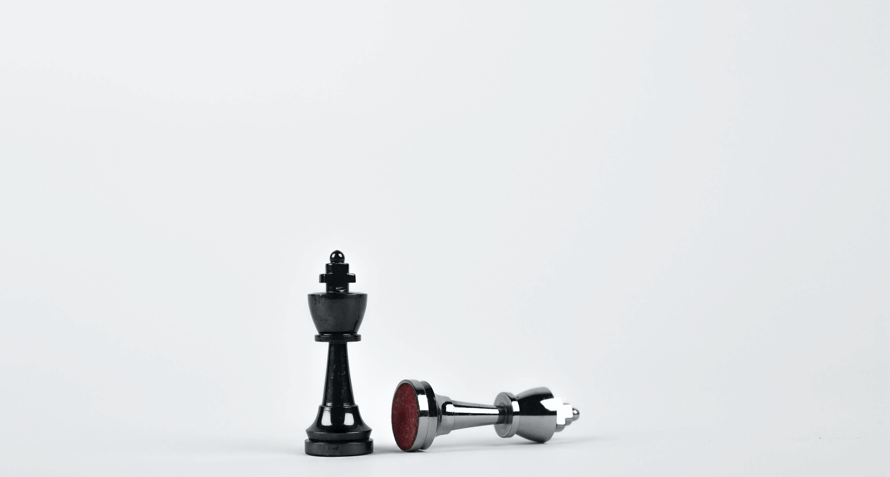 A standing black chess king beside a toppled silver chess king